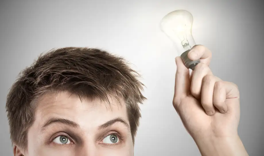 A person holds a glowing light bulb near their head, symbolizing a new idea or inspiration—such as discovering ways to avoid challenges to your estate plan—against a neutral gray background.