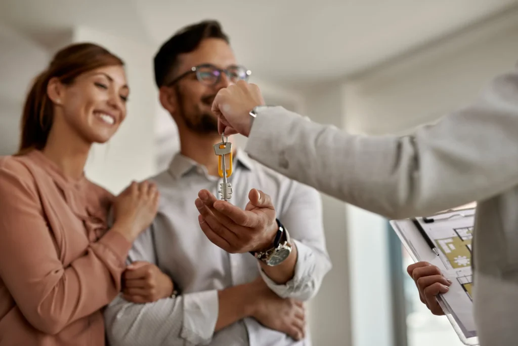 A person hands a set of house keys to a smiling couple, with one holding a clipboard and floor plan—an exciting step often involved in Residential Real Estate Litigation in South Carolina.