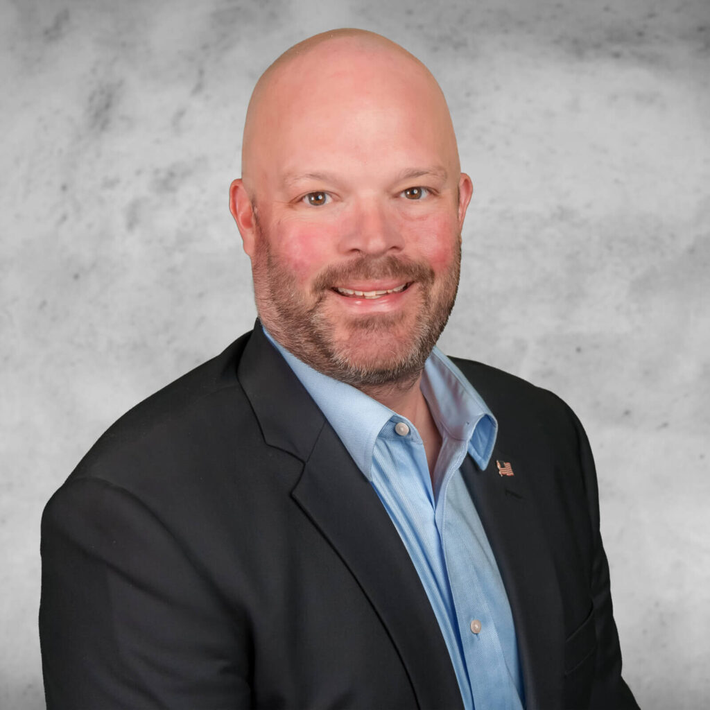 Bobby Sawyer, a man with a beard, smiles warmly in a dark blazer and light blue shirt against a gray marbled background.