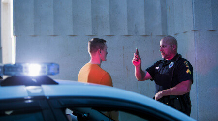 A police officer conducts a sobriety test on a man beside a police car at night.